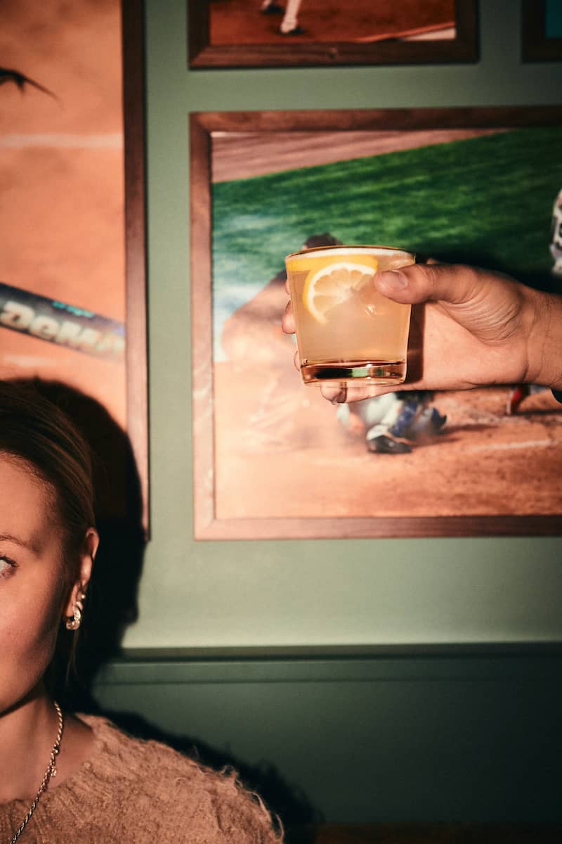 En hand som håller i en orange drink med en skiva citrusfrukt i